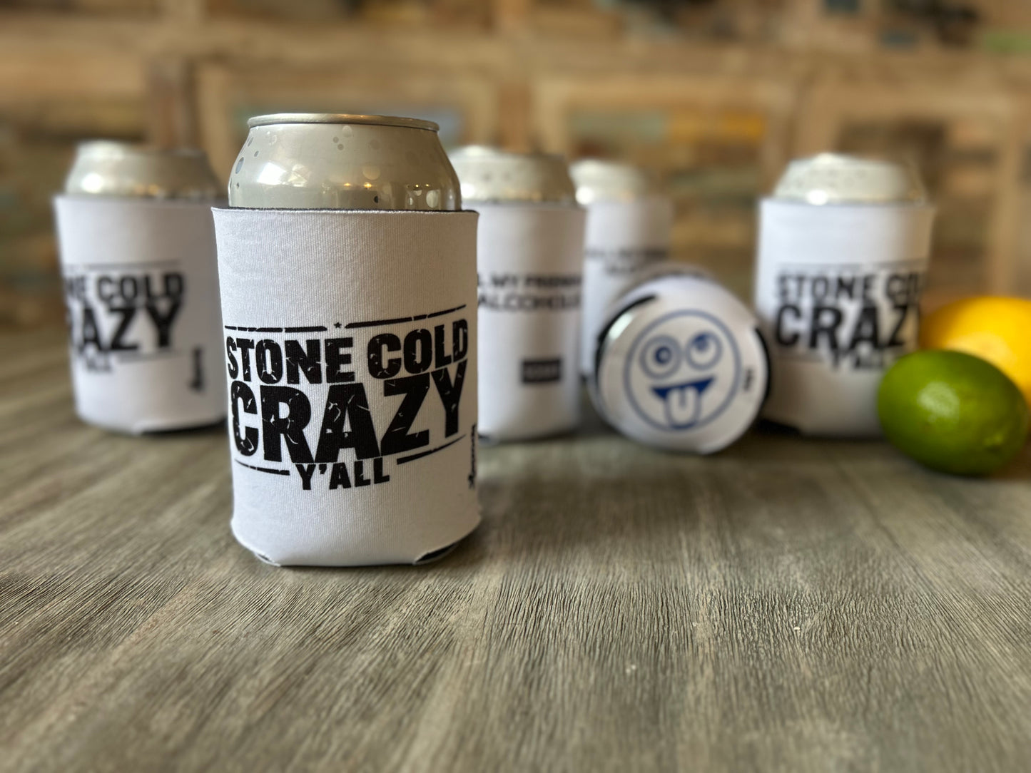 Can coolers with 'Stone Cold Crazy Y'all' text on a wooden surface with limes and lemons.