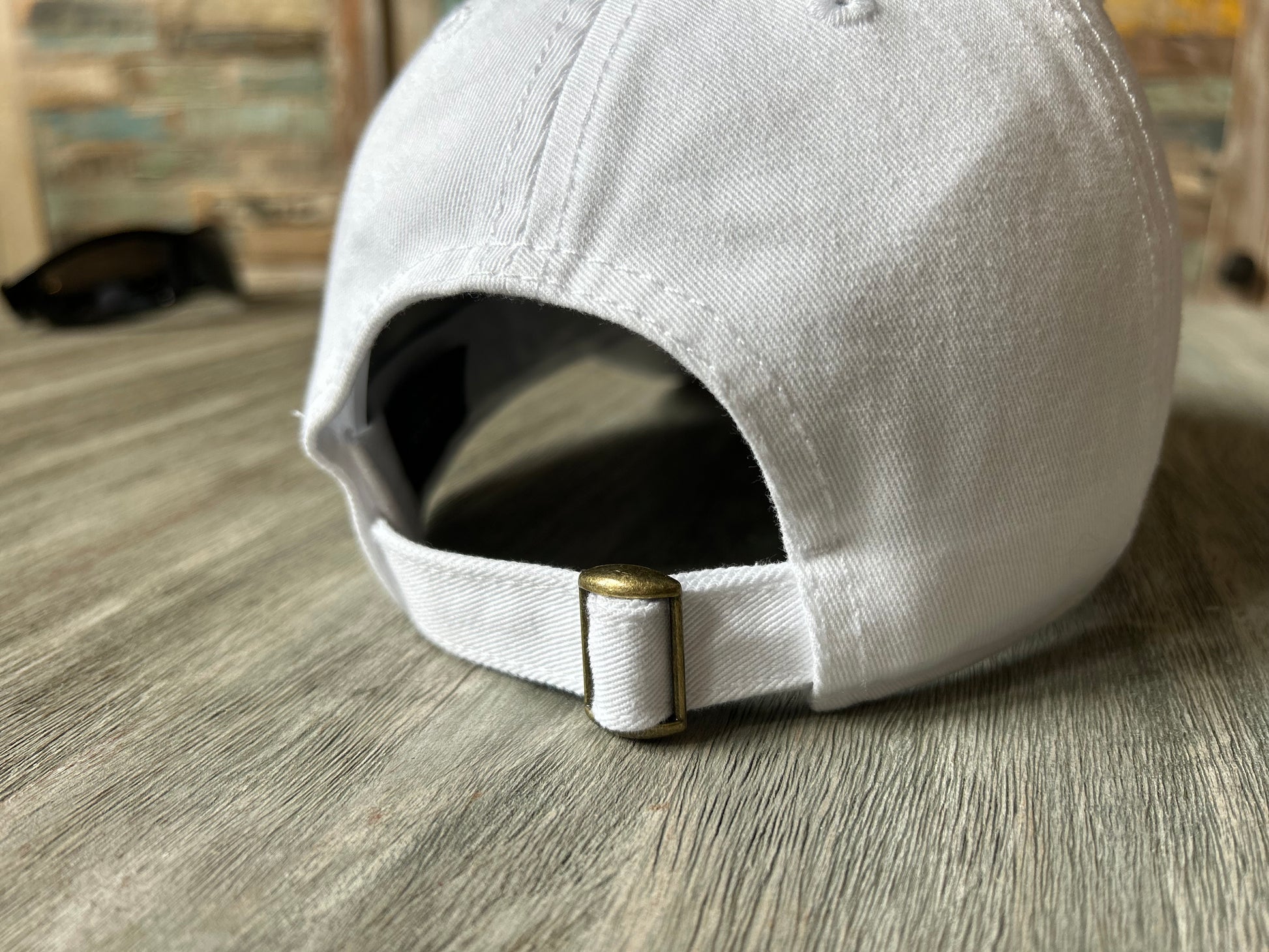 White baseball cap with a gold buckle on a wooden surface