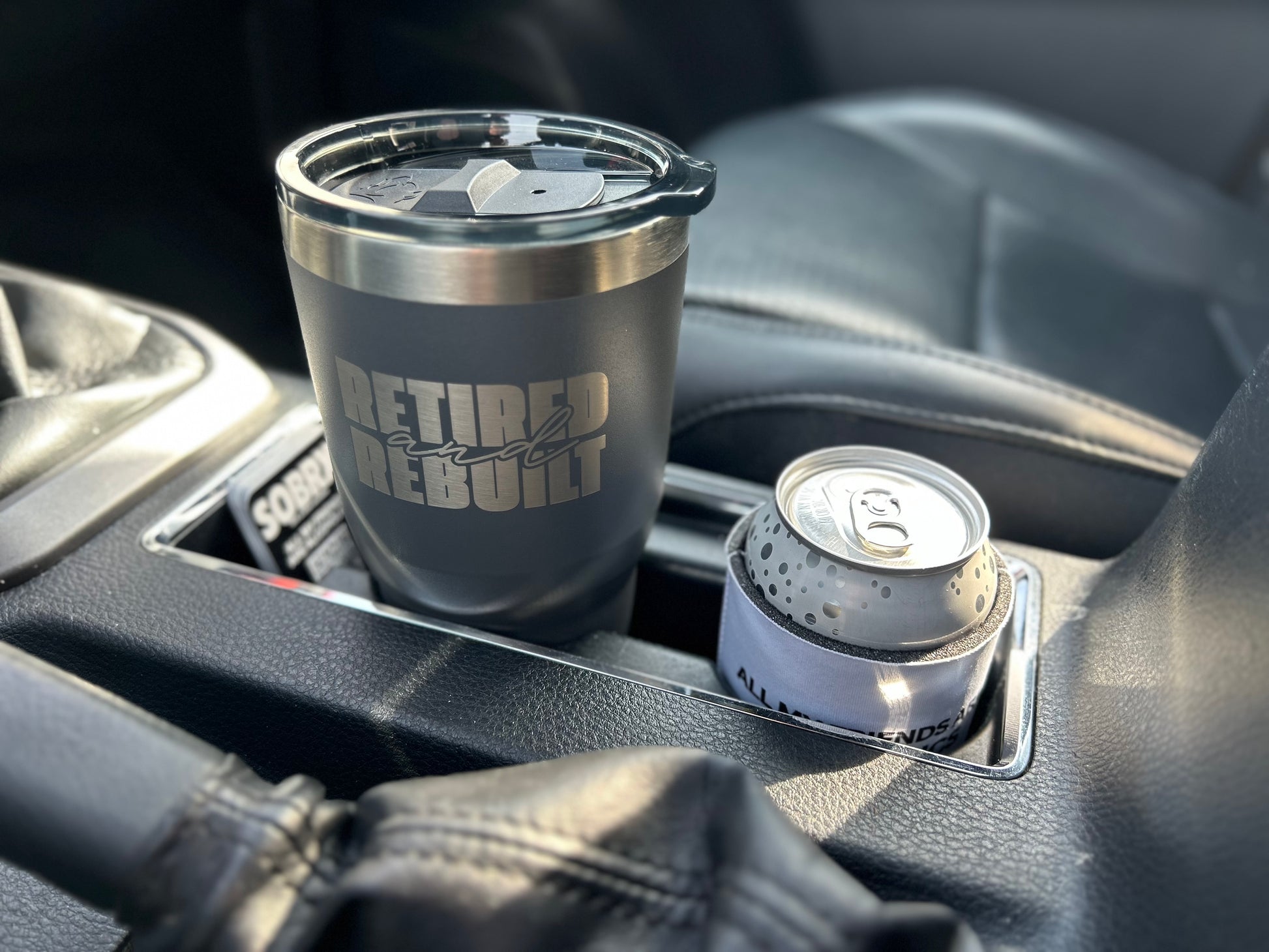 Gray tumbler with 'Retired and Rebuilt' text in a car cup holder.