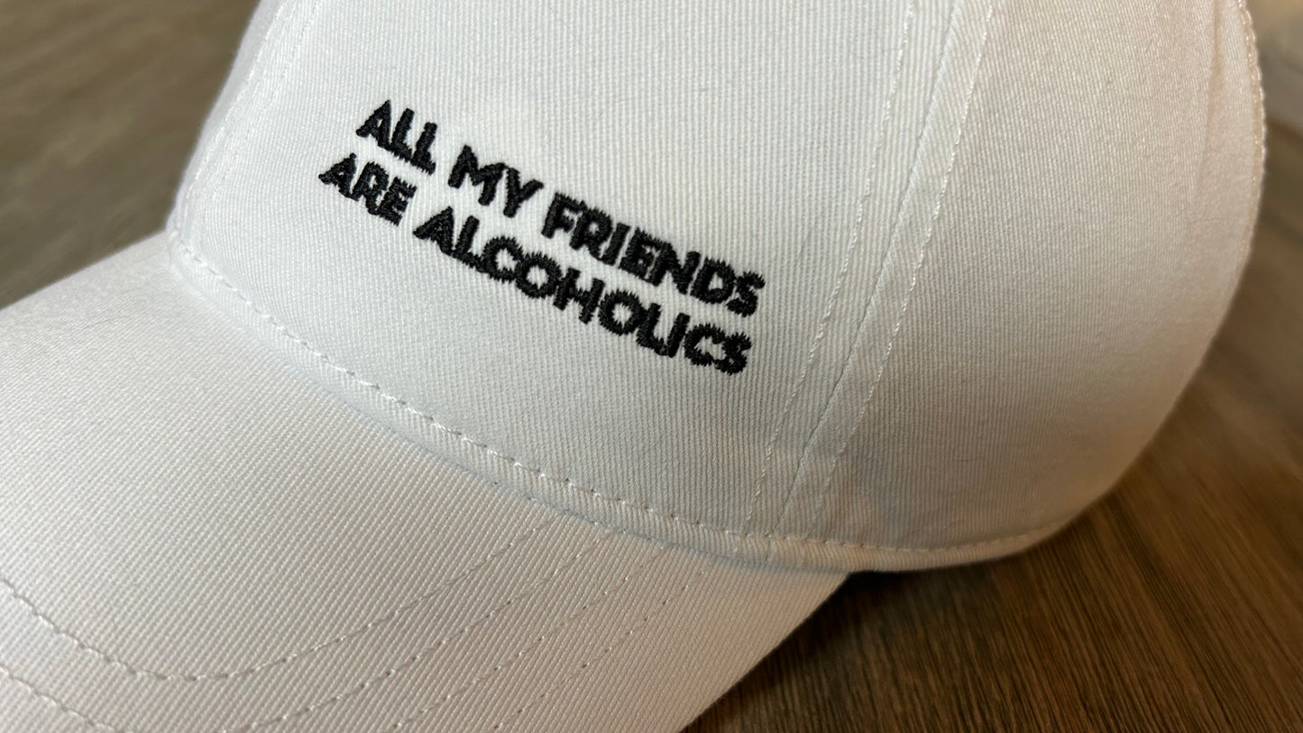 White cap with black text 'All My Friends Are Alcoholics' on a wooden surface